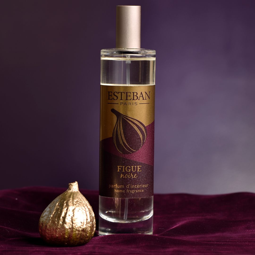Parfum d’intérieur Esteban Paris Figue Noire en spray, flacon vaporisateur transparent avec étiquette prune et dorée, présenté sur un tissu violet aux côtés d’une figue décorative dorée