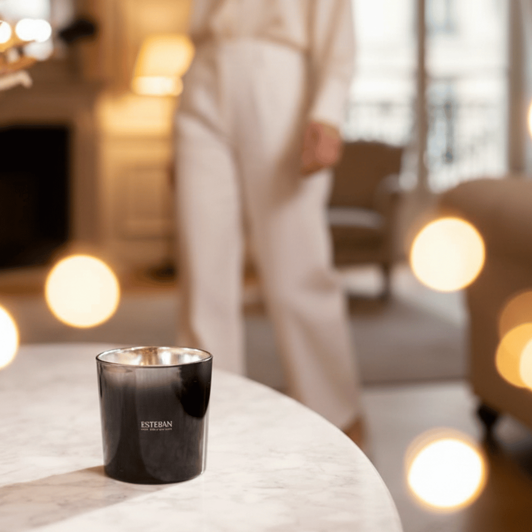 Bougie parfumée Esteban Paris en verre fumé noir, présentée sur une table en marbre dans un intérieur chaleureux avec éclairages d’ambiance et arrière-plan flou