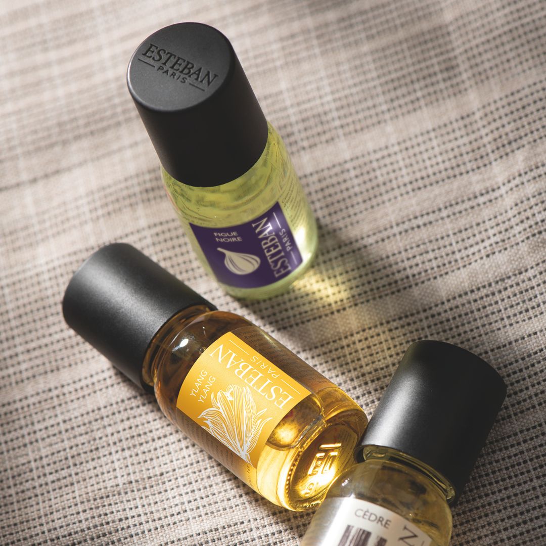 Huiles parfumées Esteban Paris Ylang-Ylang, Figue Noire et Cèdre, flacons concentrés de parfum présentés sur un tissu texturé dans une ambiance chaleureuse et élégante